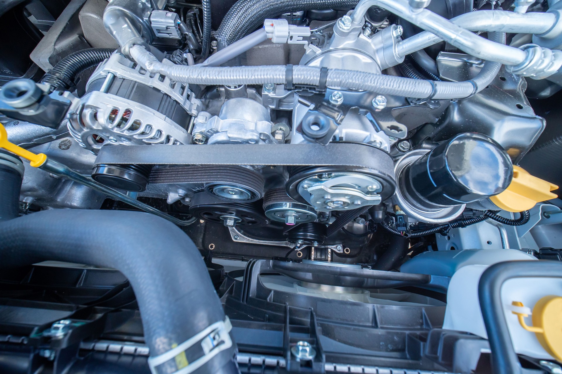 Close up view of engine block timing cover with pulley water pump, rubber belt, tubes and hoses. Engine oil dipstick on the side. Under the hood engine compartment inspection.