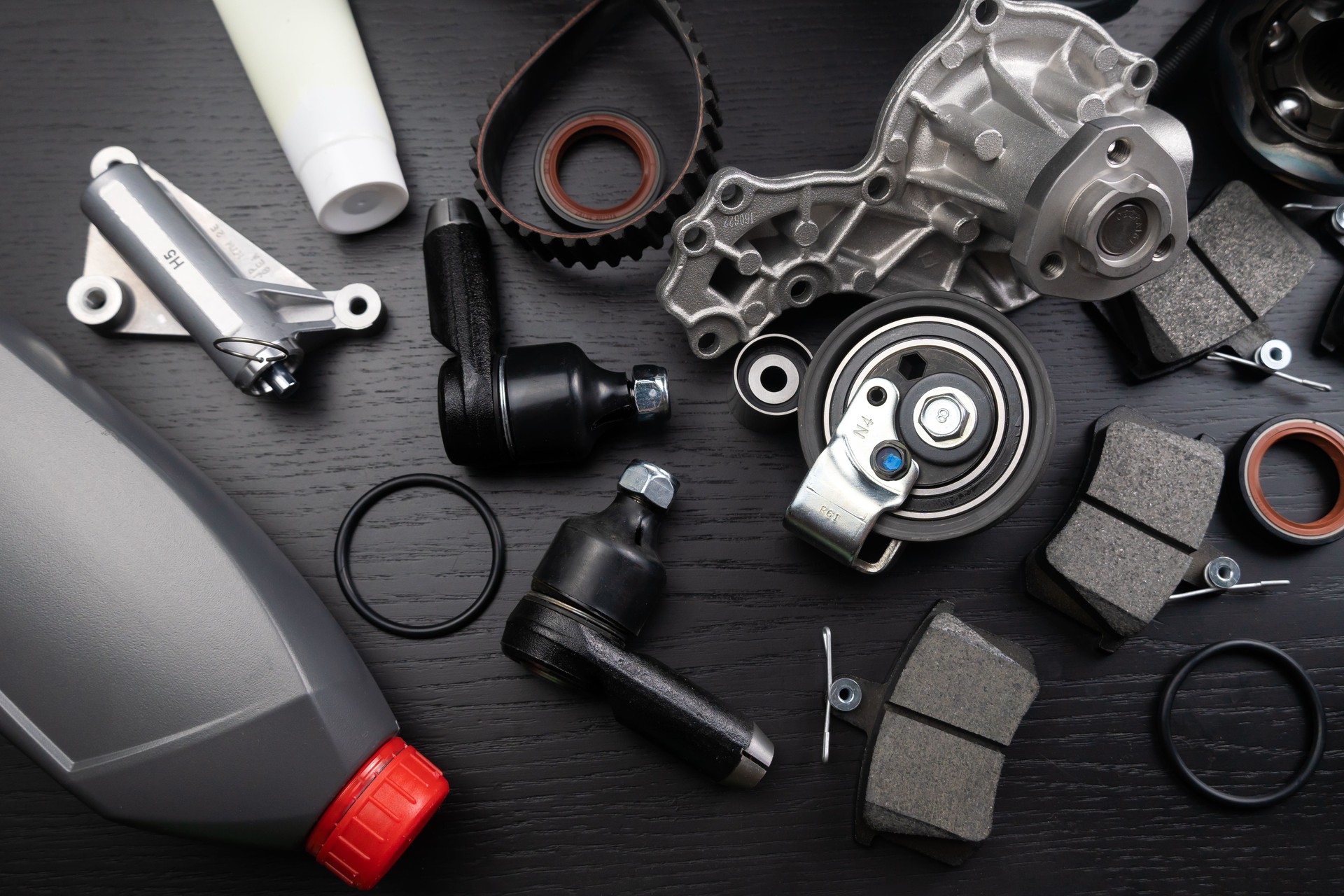 Muchas piezas de automóviles se encuentran sobre un fondo negro de madera. Piezas del motor y la suspensión, nudillo giratorio, juntas y piezas del motor desplegadas. Piezas de repuesto nuevas. Rumbos. Juega con la luz. Colgado sobre la mesa.